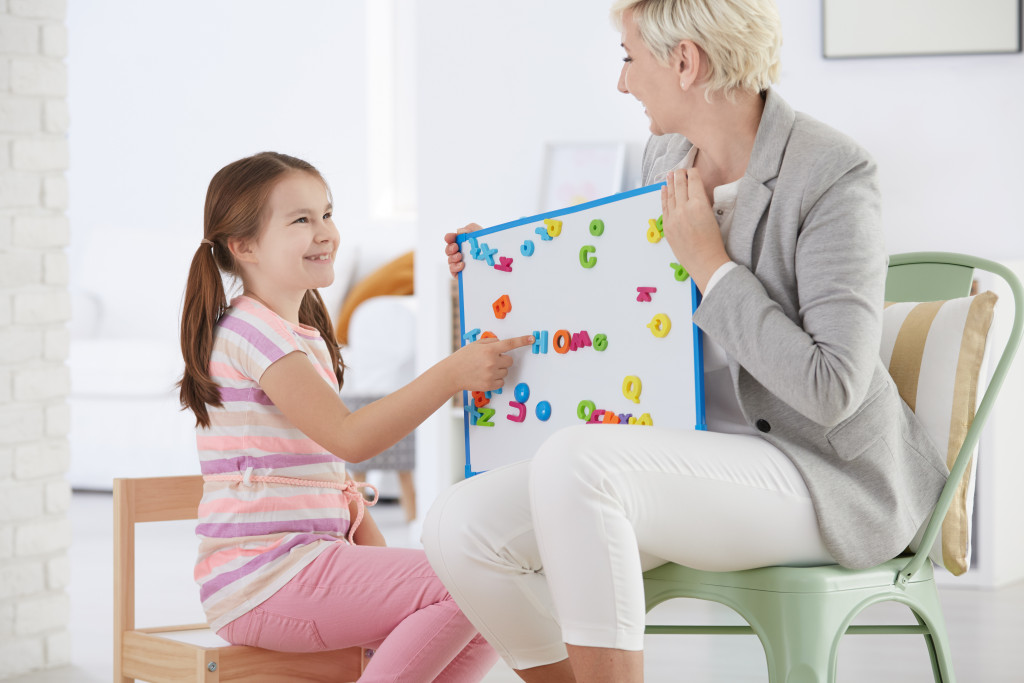 woman holding alphabet board teaching girl child