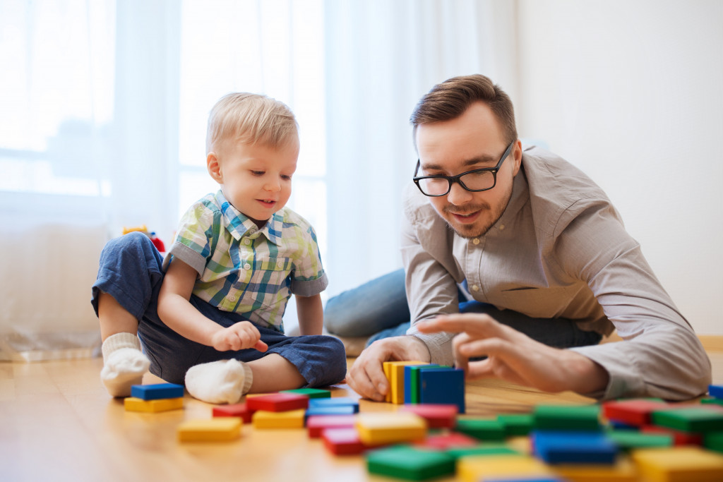 Single father playing with blocks with his young son on the floor.