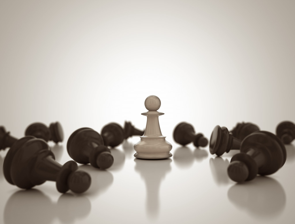A single standing white chess piece among toppled down black pieces